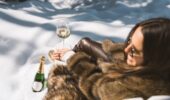 A woman wearing a fur coat enjoying apres ski with a glass of wine