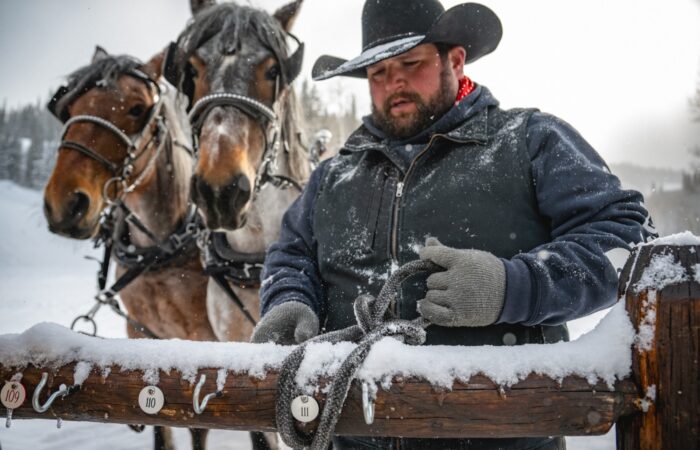 A man tying two horses to a wooden fence at Deer Valley