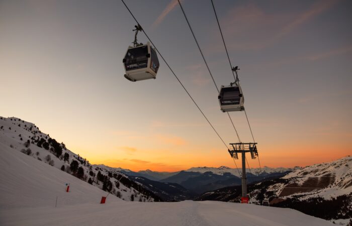 Ski chairlift over snow-covered mountains at sunset in Méribel, France.