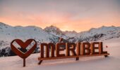 Méribel ski resort logo on snowy slopes at sunset in the French Alps.