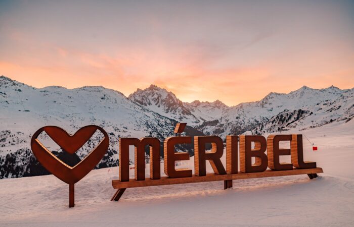 Méribel ski resort logo on snowy slopes at sunset in the French Alps.