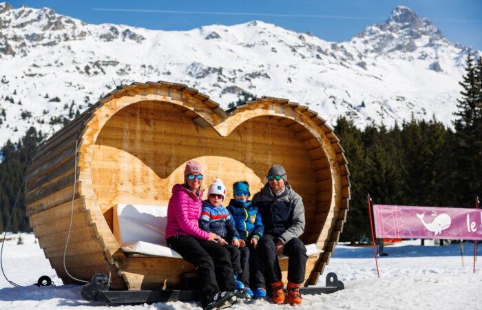 Family posing in the iconic heart seat in Méribel, France during a winter ski holiday.