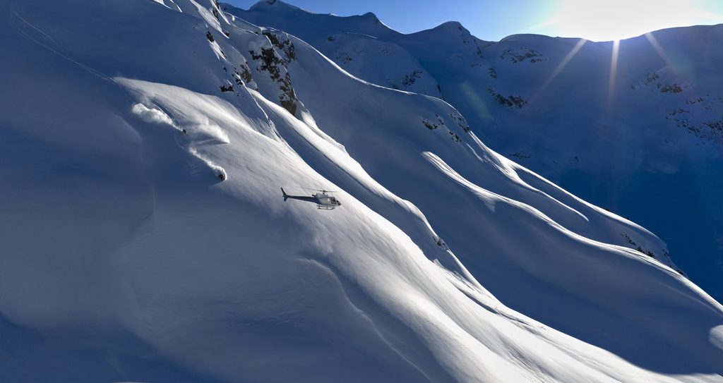 A helicopter flying past snow covered mountains with heli skiiers on board