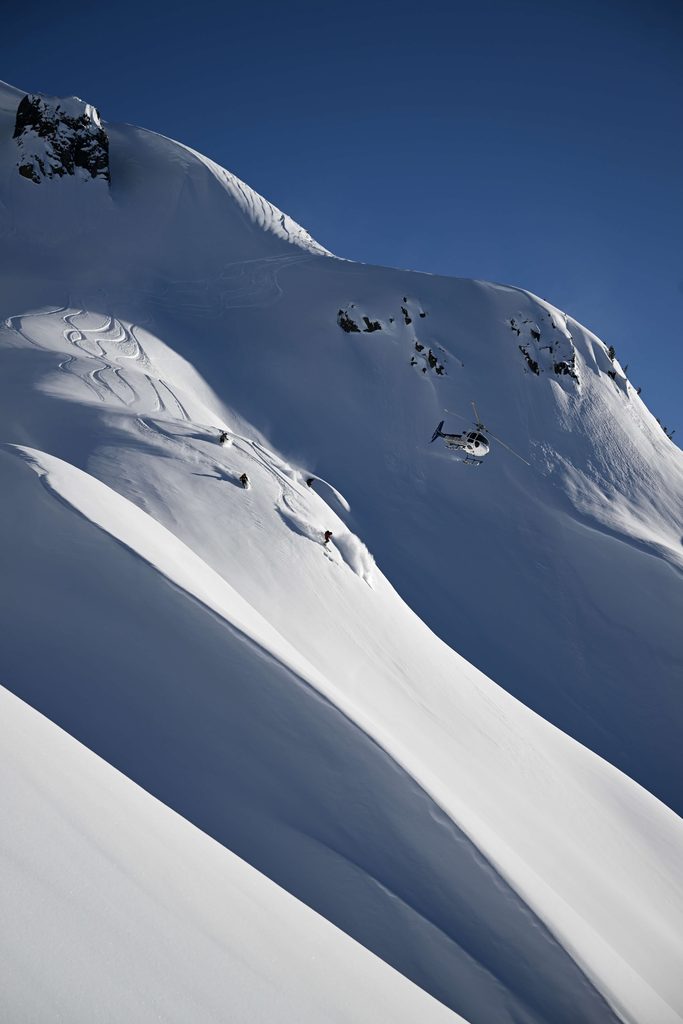 A helicopter flying past snow covered mountains with heli skiiers on board