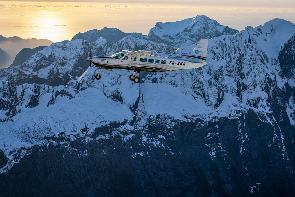 A small plane flying against a backdrop of snow topped mountains