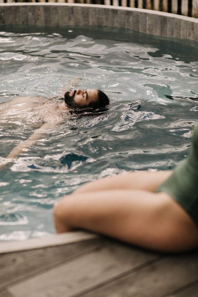 A man floating on his back while a woman sits on the side of the pool at Bathe by Aluume Queenstown
