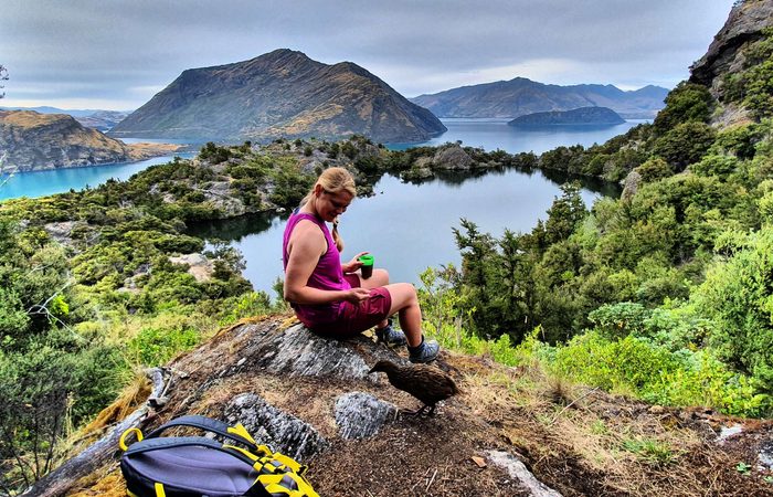 A hiker having a coffee breat on top of a rocky outcrop overlooking a lake